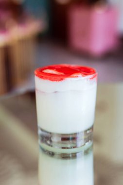 Üstünde çilek köpüğü olan kremalı bir kokteyl. Buzlu bardakta servis ediliyor.