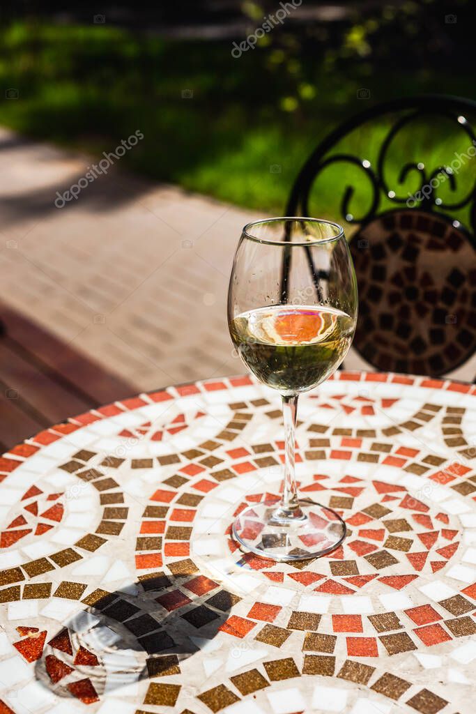 A glass of white wine on a mosaic stone table of a cafe terrace on a sunny day
