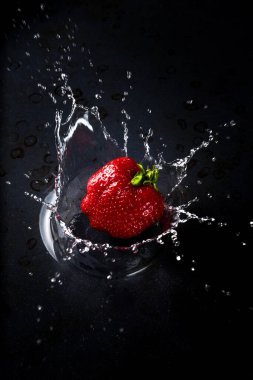Suya düşen taze bir çilek. Büyük bir sıçrama, koyu bir arka plan.