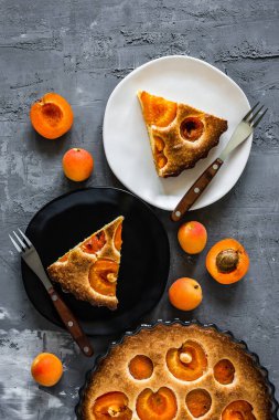 Kayısı turtası, beyaz ve siyah bir tabak, turta, çatal ve kayısı parçaları. Gri arkaplan, üst görünüm