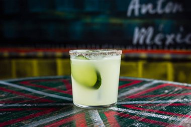 Büyük bir buzlu buzlu bardakta salatalık dilimiyle süslenmiş, cam kenarında baharatlı bir kokteyl.