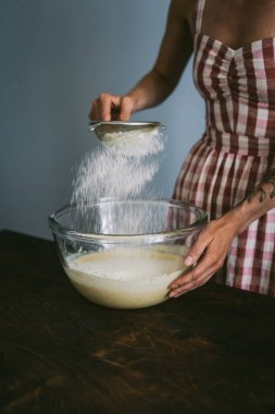 Belarus, Minsk - 08.03.2020: Kırmızı ve beyaz elbiseli genç kadın kek pişiriyor, unu diğer malzemelerle karıştırıyor.