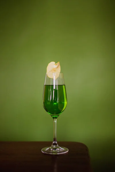 一种绿色鸡尾酒 装在长笛玻璃杯中 用脱水的苹果片装饰在绿色背景上 — 图库照片