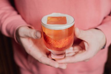 Güzel pembe bir kokteyl. Alçak bardakta büyük bir buz küpü. Kan portakalı hazzıyla süslenmiş. 