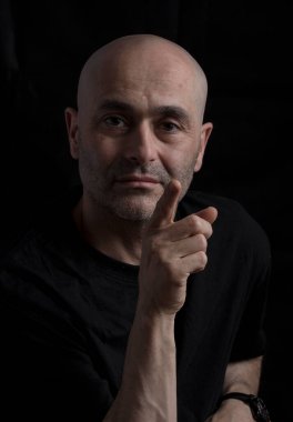 Siyah arka planda kameraya bakan bir adam.