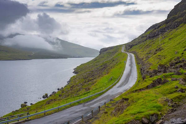 Danimarka, Avrupa 'da Faroe Adaları' nda bir gölün sınırında ıslak bir yol. Yağmurlu bulutlu bir gün. Güzel bir manzara.