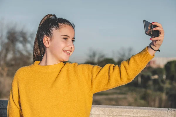 Sarı kazaklı kız parkta selfie çekiyor. Teknoloji, gençlik, doğa kavramı