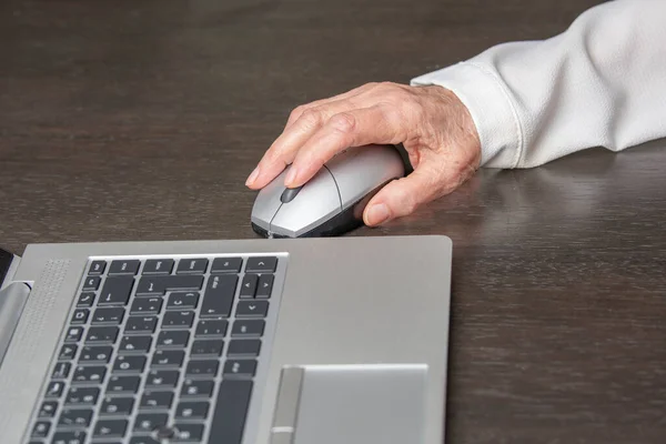 old lady using a laptop mouse on a wooden table. technology concept, learning, health, vitality