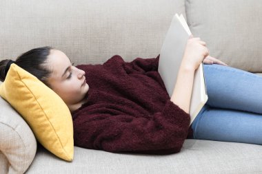 Kanepede uzanmış boş sayfalarla kitap okuyan bir kız.