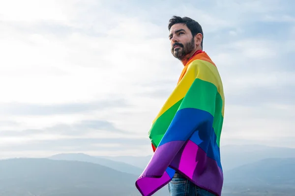 Gökyüzünde eşcinsel bayrağı olan yakışıklı bir adam. Gay, gurur, çeşitlilik kavramı.