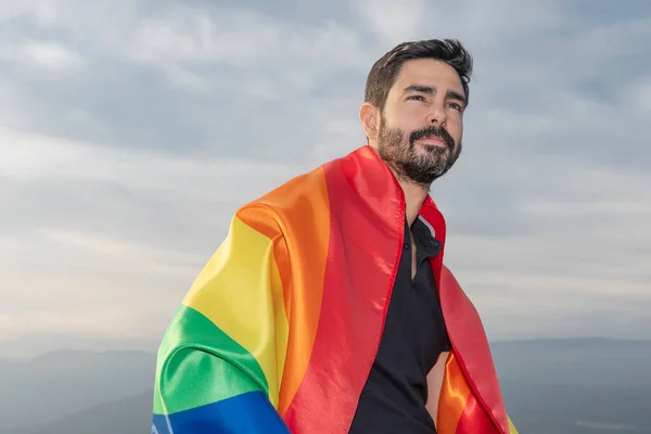 Gay gülüşü, gay bayrağıyla oturmuş ufka bakıyor. Gey, gurur, çeşitlilik kavramı.