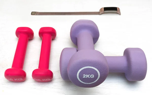 Beyaz arka planda dijital saatin yanında farklı ağırlıkta ve renkte dambıllar. fitness konsepti