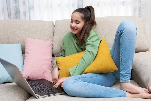 Girl smiling on a couch looking at a laptop with several colorful cushions