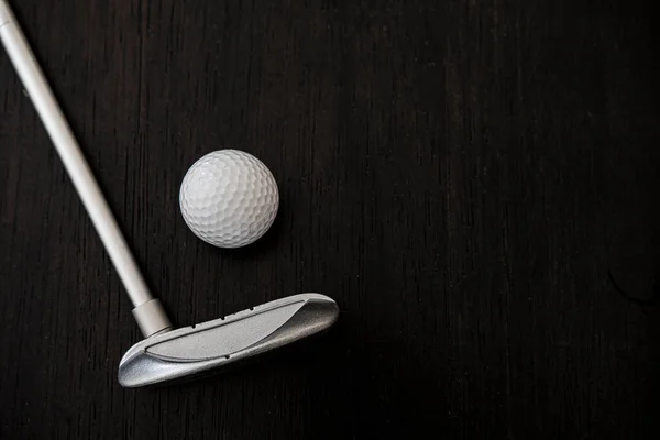 Siyah ahşap arka planda golf topunun yanındaki metal golf sopası.