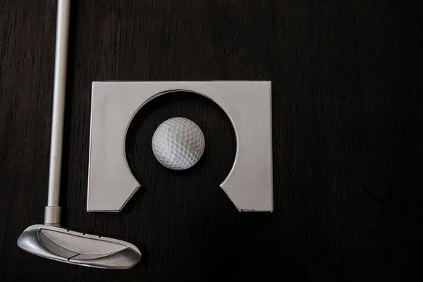 Golf topunun yanındaki metal golf sopası ve siyah ahşap arka planda oynamak için delik çerçeve.
