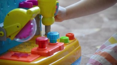 Bir kız (çocuk) yerde oturur ve bir oyuncak matkabın koluna basar. Matkabın üzerinde bir ışık yanıyor. Yüzü görünmüyor. Yakın plan.