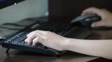 Çocuk bilgisayara bağlandı. Sol el siyah klavyenin üzerinde duruyor. Sağ el fareyi tutuyor