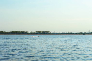 Yaz, sıcak. Nehirde bir kadın mobiletle geziyor. Arkanızda bir tren yolu, bir otoyol ve bir elektrik santrali görebilirsiniz.