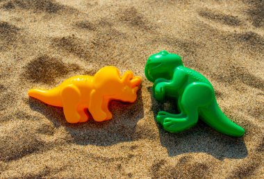 Yeşil ve sarı bebek dinozor kalıpları kumun üzerinde yatıyor. Yakın plan.