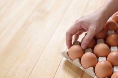 Açık kahverengi ahşap arka planda tavuk yumurtası toplayan bir el, boşluğu kopyala