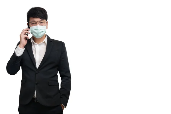 アジアのビジネスマンは 正式な黒いスーツのジャケットで外科用フェイスマスクを身に着けています 右手で話をするスマートフォンを使用して カメラを見て スタジオ照明は白い背景に隔離 コロナウイルスのための概念 Covid19 — ストック写真