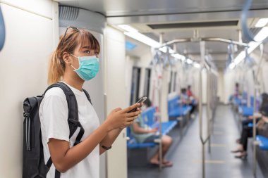 Asyalı genç bir sırt çantalı kadın metroyla ya da Skytrain 'le şehre giderken maske takıyor. COVID-19 konsepti.