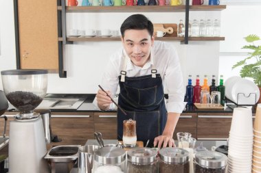 Genç gülümseyen Asyalı kahveci kahve yapıyor. Kahve dükkanındaki kameraya bakıp mutlu oluyor.