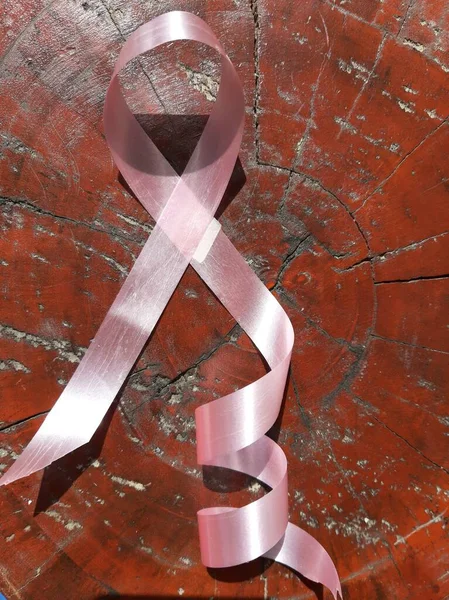 Göğüs kanseri kavramı: Kahverengi ahşap arka planda göğüs kanserinin pembe kurdele sembolü.