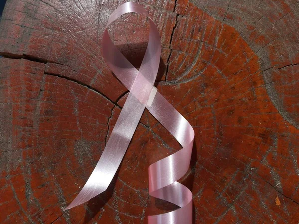 Göğüs kanseri kavramı: Kahverengi ahşap arka planda göğüs kanserinin pembe kurdele sembolü.