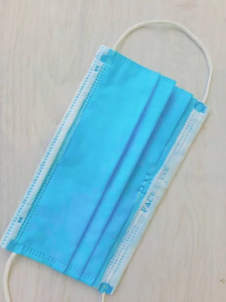 Beyaz ahşap bir arka plana yapıştırılmış koruyucu maske ağız ve burnunu örtmek için General 3 katmanlı bir maske. Bakteriyel maskeleme konsepti kulaklıklı cerrahi maske. COVID 19