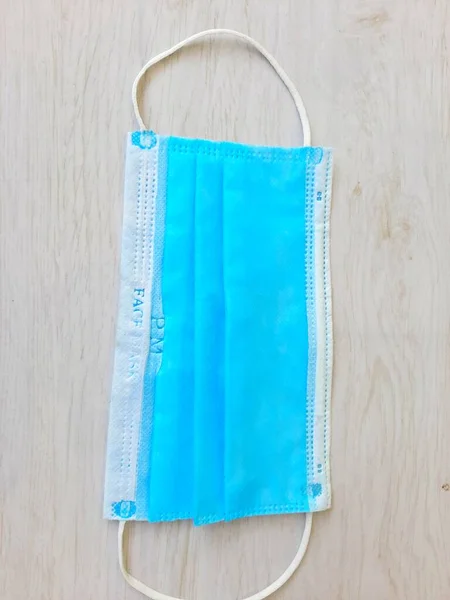 Beyaz ahşap bir arka plana yapıştırılmış koruyucu maske ağız ve burnunu örtmek için General 3 katmanlı bir maske. Bakteriyel maskeleme konsepti kulaklıklı cerrahi maske. COVID 19