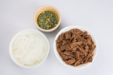 Bir kase dilimlenmiş sığır filetosu, bir tabak selofan cam erişte ve beyaz bir zemine batırılmış Vietnam Nuoc Cham sosu.