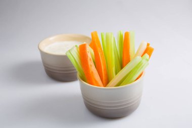 Karmaşık portakal dilimleri ve sulu yeşil kereviz çubukları ile beyaz arka planda beyaz bir kase küflü peynir sosu.