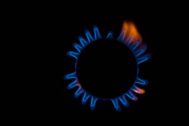 Mutfak gaz sobasından çıkan küçük alevlerle mavi ve turuncu dairesel bir ateşin yakın plan görüntüsü ve siyah arka planda bir melek ya da kaplumbağa silueti oluşturur.