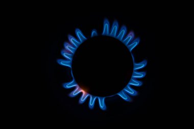 Mutfak gaz sobasından çıkan küçük alevlerle mavi ve turuncu dairesel bir ateşin yakın plan görüntüsü ve siyah arka planda bir melek ya da kaplumbağa silueti oluşturur.