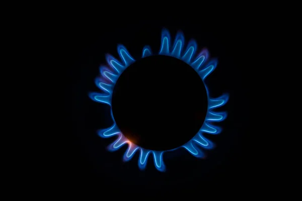 Mutfak gaz sobasından çıkan küçük alevlerle mavi ve turuncu dairesel bir ateşin yakın plan görüntüsü ve siyah arka planda bir melek ya da kaplumbağa silueti oluşturur.