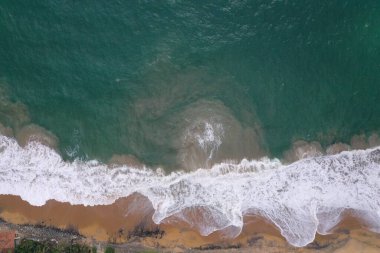 Turkuaz mavi su, büyük beyaz dalgalar ve köpük, sarı kumlu boş plaj, siyah kayalar, güzel dokular, desenler ve şekiller oluşturan deniz uçağı görüntüsü. Sri Lanka