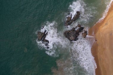 Turkuaz mavi su, büyük beyaz dalgalar ve köpük, sarı kumlu boş plaj, siyah kayalar, güzel dokular, desenler ve şekiller oluşturan deniz uçağı görüntüsü. Sri Lanka