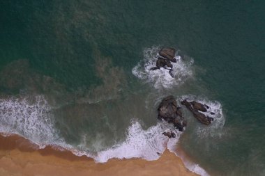 Turkuaz mavi su, büyük beyaz dalgalar ve köpük, sarı kumlu boş plaj, siyah kayalar, güzel dokular, desenler ve şekiller oluşturan deniz uçağı görüntüsü. Sri Lanka