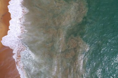 Turkuaz mavi su, büyük beyaz dalgalar ve köpük, sarı kumlu boş plaj, siyah kayalar, güzel dokular, desenler ve şekiller oluşturan deniz uçağı görüntüsü. Sri Lanka