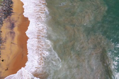 Turkuaz mavi su, büyük beyaz dalgalar ve köpük, sarı kumlu boş plaj, siyah kayalar, güzel dokular, desenler ve şekiller oluşturan deniz uçağı görüntüsü. Sri Lanka