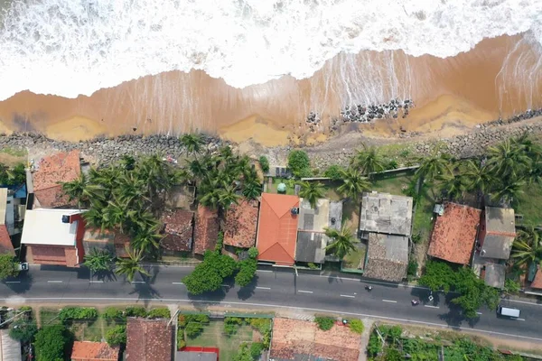 natural aerial drone bird view day shot of the sea shore with beautiful villas, green trees, yellow sand and big white waves and foam crashing on the beach. Pitiwella, Sri Lanka