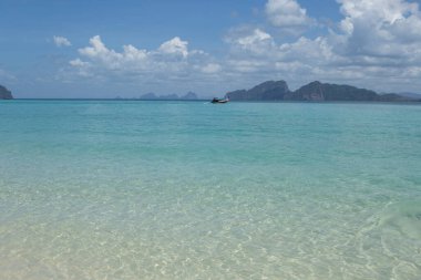 Kristal berrak, sakin, turkuaz, vahşi adalı okyanus suları ormanlı tepeler, açık mavi gökyüzü ve arka planda beyaz bulutlar. Koh Kradan, Tayland