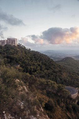 Puig de Maria tapınağı ve manastırının güzel dağları ve arkasında beyaz pembe bulutlar bulunan mavi gökyüzü olan yeşil Sant Marti tepelerinin tepesinde dikey bir yaz öğleden sonrası çekimi.
