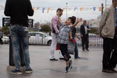 ISTANBUL / TURKEY - 30 / 05 / 2015: Uçan sabun baloncuklarını yakalamak için kolları açık havaya atlayan mutlu, genç bir Türk çocuğunun çekimi. İstanbul 'un şehir merkezindeki sokaklarda çekildi