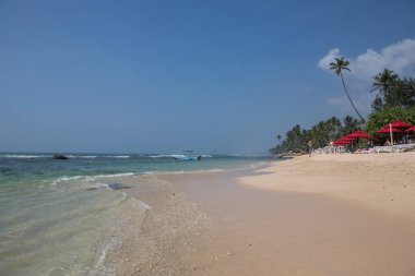 POLHENA / SRI LANKA - 15 / 01 / 2019 Deniz manzaralı cennet beyaz kumsal, kristal berrak mavi okyanus suyu, küçük dalgalar, yeşil palmiye ağaçları ve kıyıdaki barakalar