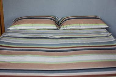 Renkli, çizgili, iki yastıklı bir çarşafın iç doğal ışık görüntüsü, çift kişilik bir yatağın üzerinde tekstil pamuklu bir yorgan.