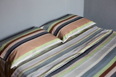 Renkli, çizgili, iki yastıklı bir çarşafın iç doğal ışık görüntüsü, çift kişilik bir yatağın üzerinde tekstil pamuklu bir yorgan.