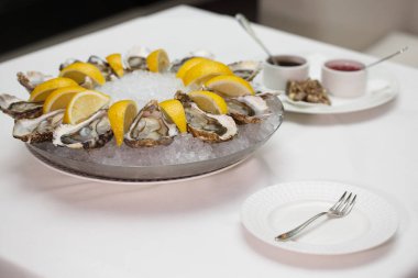 Yan manzara, taze çiğ, kabuk soyulmuş istiridyeleri mignonette shallot sirkesi ve Ponzu soslarının yanında, soğuk bir buz tepsisinin üzerinde duran limon dilimleri arasında yakın çekim yap.