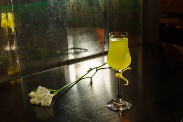 在一面肮脏的镜子背景上 在白花旁边的桌子上 放着一个透明的酒杯 里面放着一杯鲜嫩的 黄色的荔枝柠檬利口酒 — 图库照片